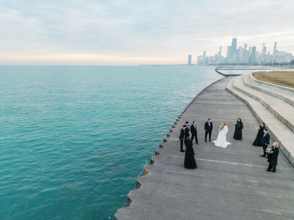 Aerial view of a bridal party taking photos by the lake with the Chicago skyline in the background